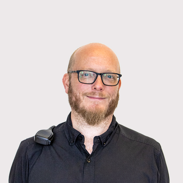 Professional headshot of a man with glasses, a beard, and a black shirt, looking directly at the camera.